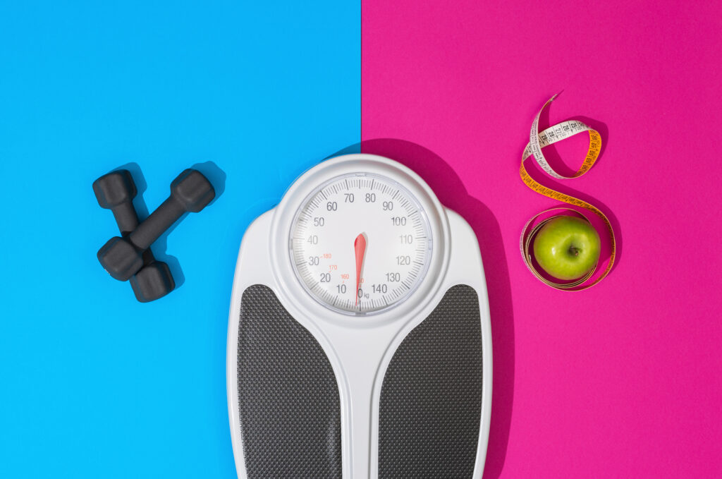 Image of a scale, weights, and a tape measure surrounding an apple indicating aspects of weight loss