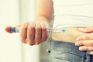Image of a woman’s hand injecting medication into her stomach
